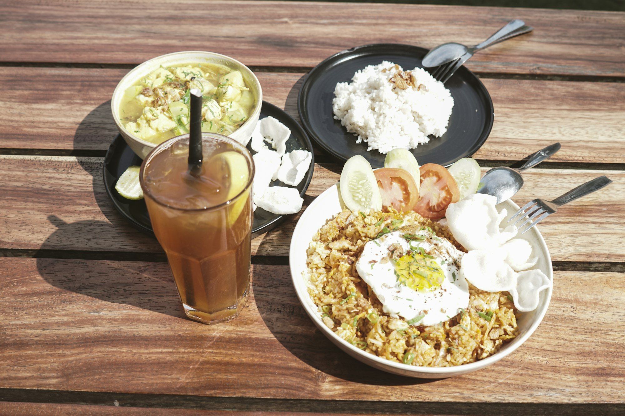 Nasi goreng dengan telur mata sapi, kerupuk, dan es teh di meja kayu